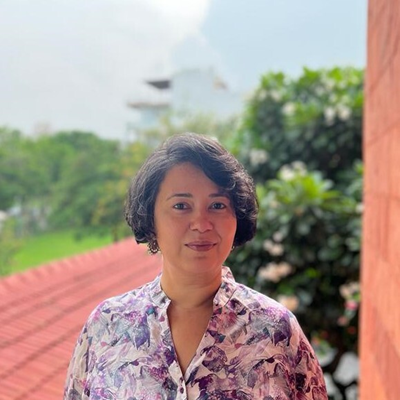 Headshot of Radhika Sen with buildings and trees in the background.
